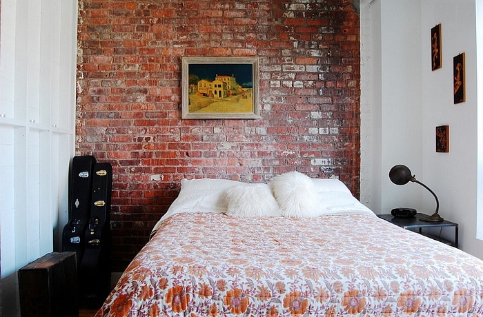 Красивая спальня украшена картинами и каменной кладкой на стене, всё это отлично подчеркивает домашнюю атмосферу.