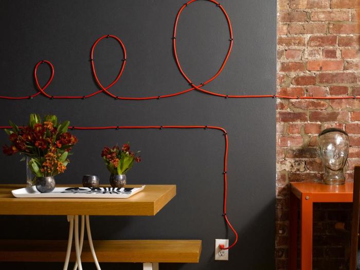Красный провод электропитания контрастным оттенком выделяется на фоне темной стены.  