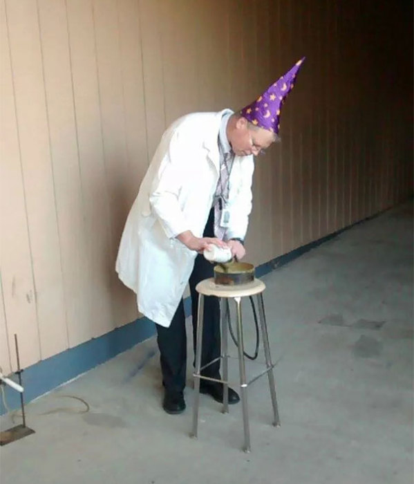 Учитель химии в шляпе волшебника проводит опыты на уроке.